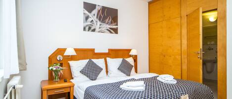A hotel room with a wooden headboard, a bed with a patterned bedspread, a nightstand with a lamp, and a painting on the wall.