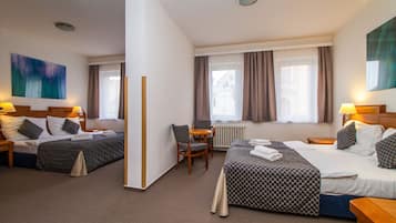 A hotel room with two beds, a small table, chairs, and a window with curtains.