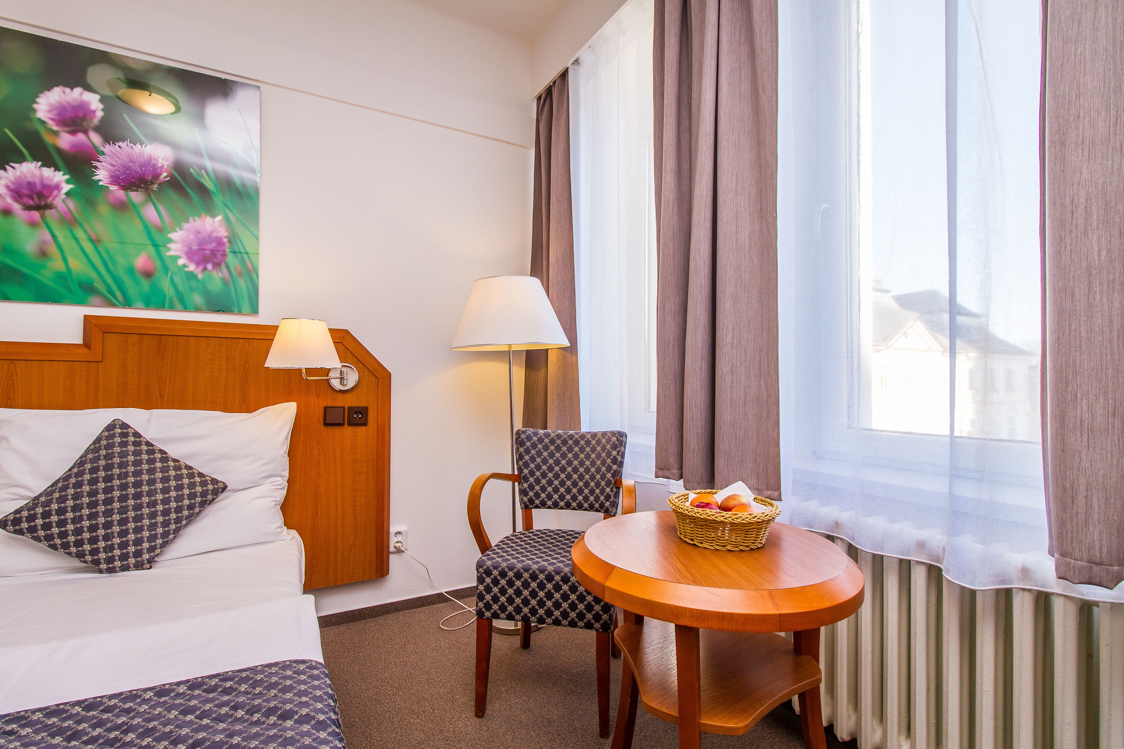 A hotel room with a bed, a chair, a table, and a window with curtains.