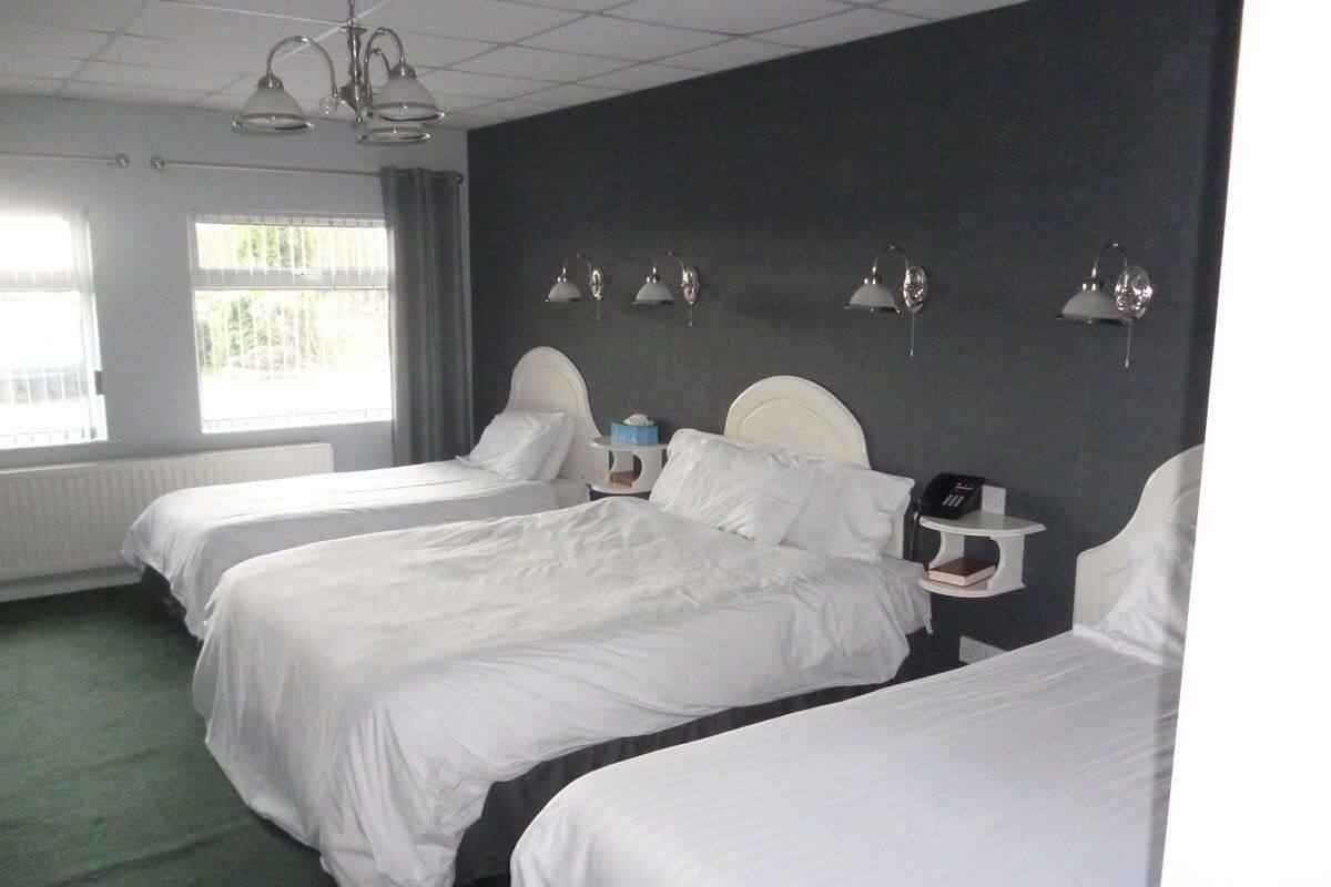 Habitación de hotel con tres camas individuales, una mesita de noche con teléfono y una ventana con cortinas.