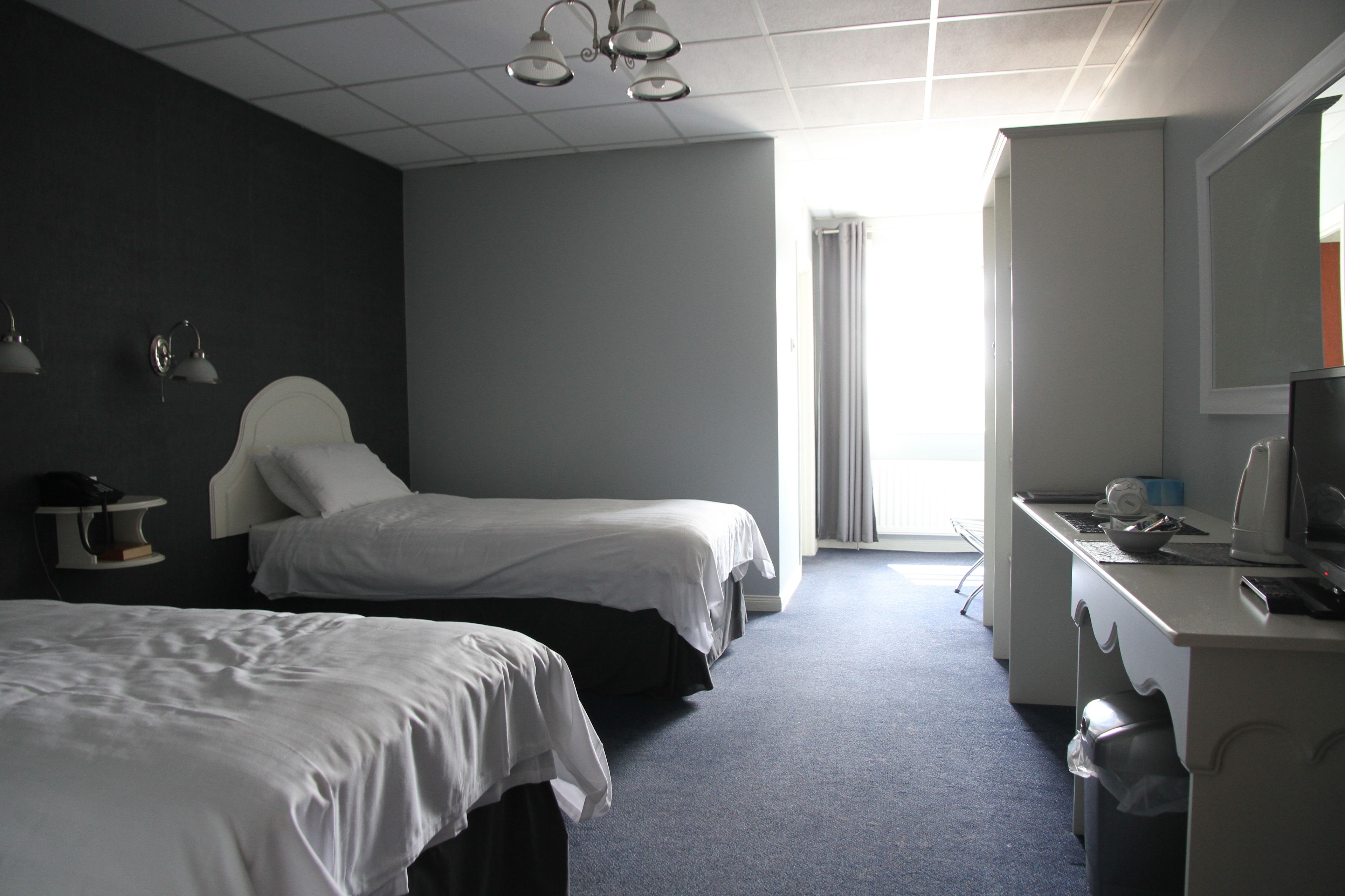 A hotel room with two beds, a desk with a computer, and a window with curtains.