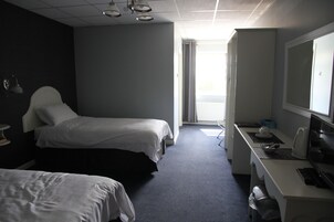 A hotel room with two beds, a desk with a computer, and a large window.
