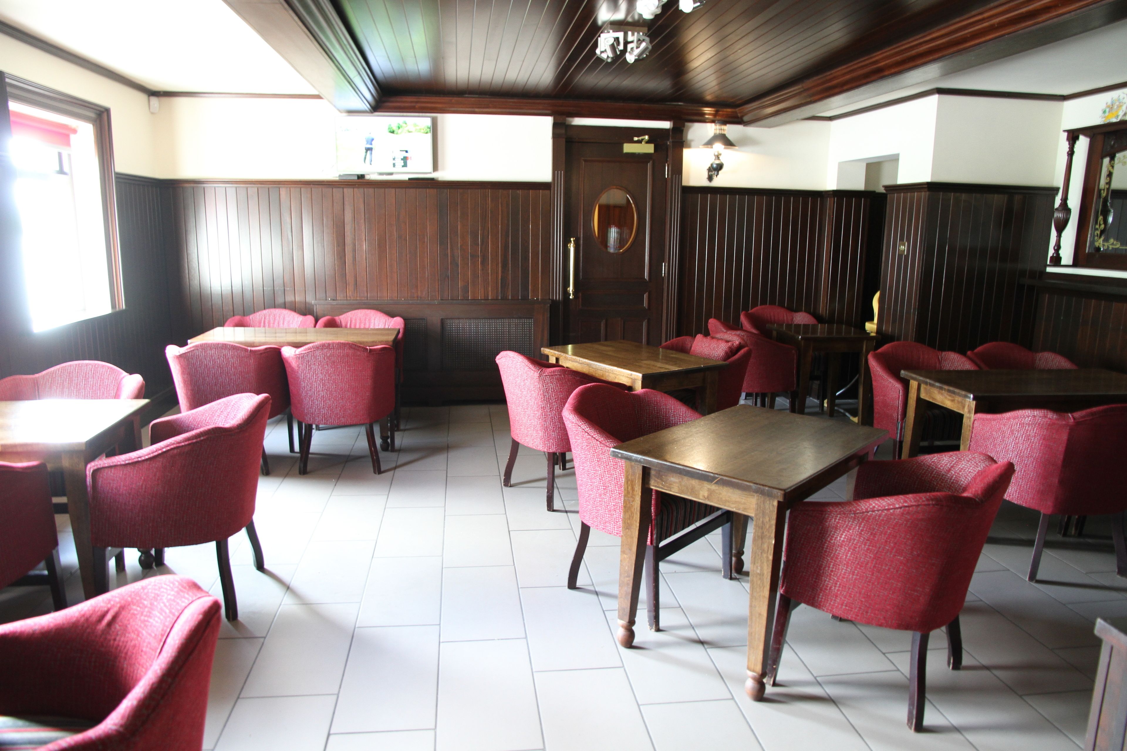 A restaurant with wooden tables and red chairs, a tiled floor, and a wooden ceiling.