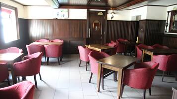 A restaurant with wooden tables and red chairs, a tiled floor, and a wooden ceiling.