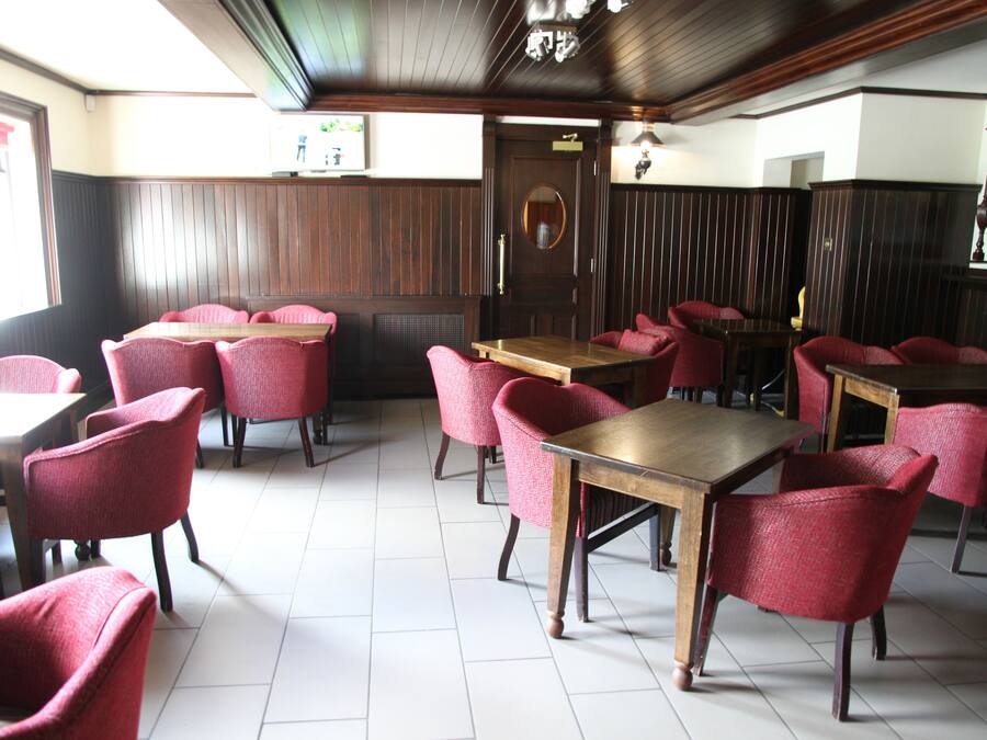 A restaurant with wooden tables and red chairs, a tiled floor, and a wooden ceiling.