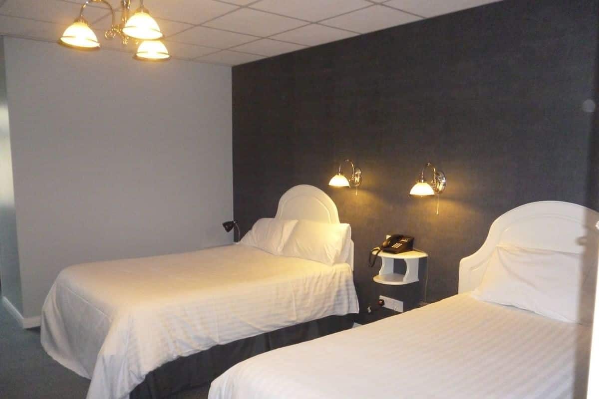 Una habitación de hotel con dos camas individuales, una mesita de noche con lámpara y un teléfono.