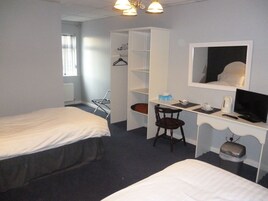 Habitación de hotel con dos camas, un escritorio con una silla, un armario y un televisor.