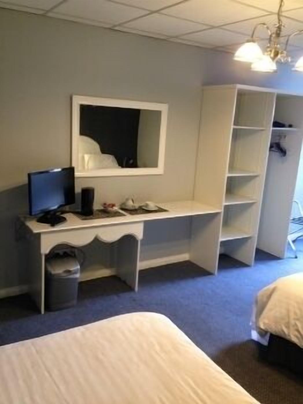 A hotel room with a bed, a desk with a computer, a mirror, and a wardrobe.