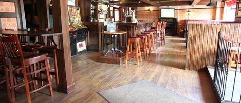 A bar area with wooden flooring, bar stools, and a counter with a television screen.