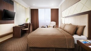 A hotel room with a large bed, a desk with a chair, a flat-screen TV mounted on the wall, and a window with curtains. - Singgasana Hotel Makassar (Makassar)