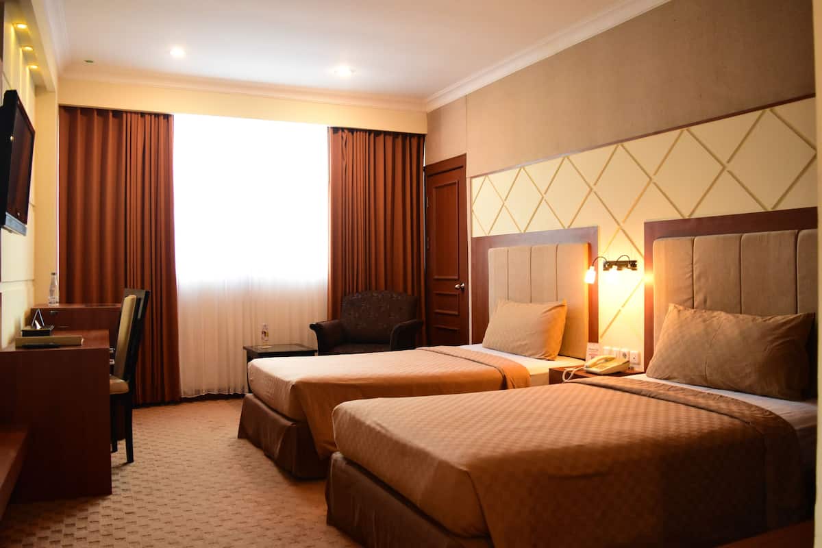 A hotel room with two beds, a desk, a chair, and a large window with curtains.