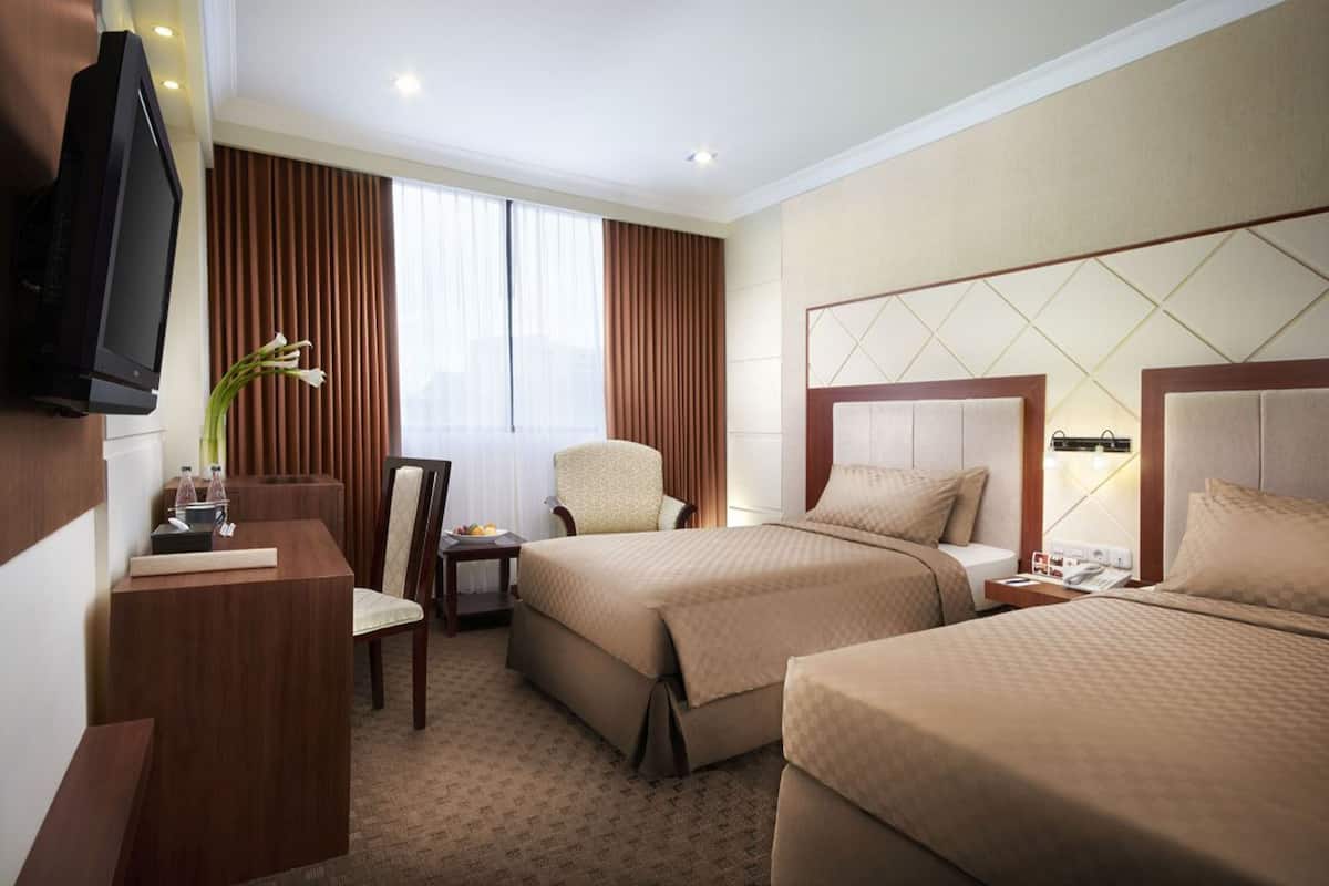 A hotel room with two beds, a desk, a chair, a TV, and a window with curtains.