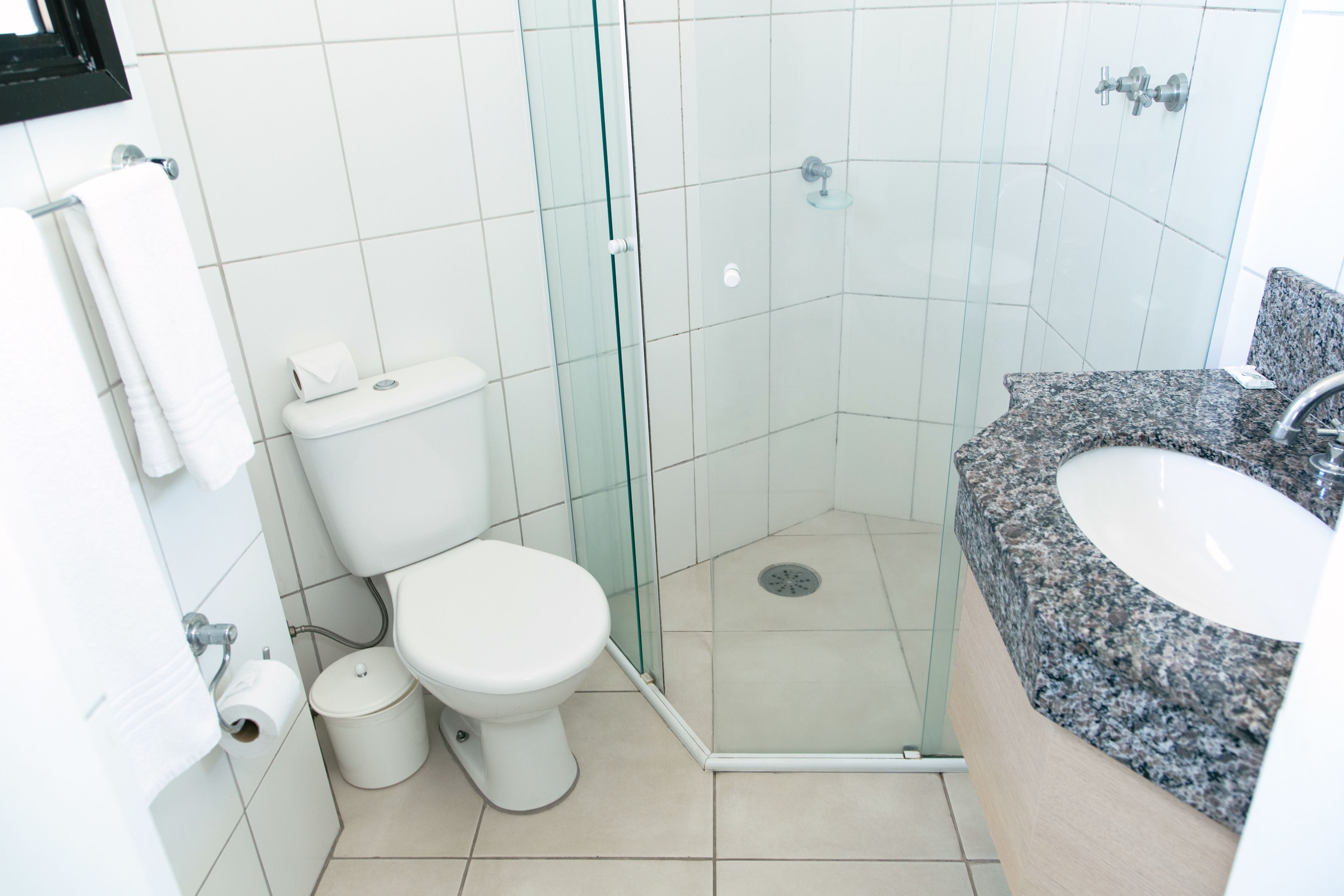 A modern bathroom with a glass-enclosed shower, a white toilet, and a granite countertop sink.