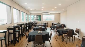 A conference room with multiple round tables and chairs, large windows, and an air conditioning unit on the ceiling.