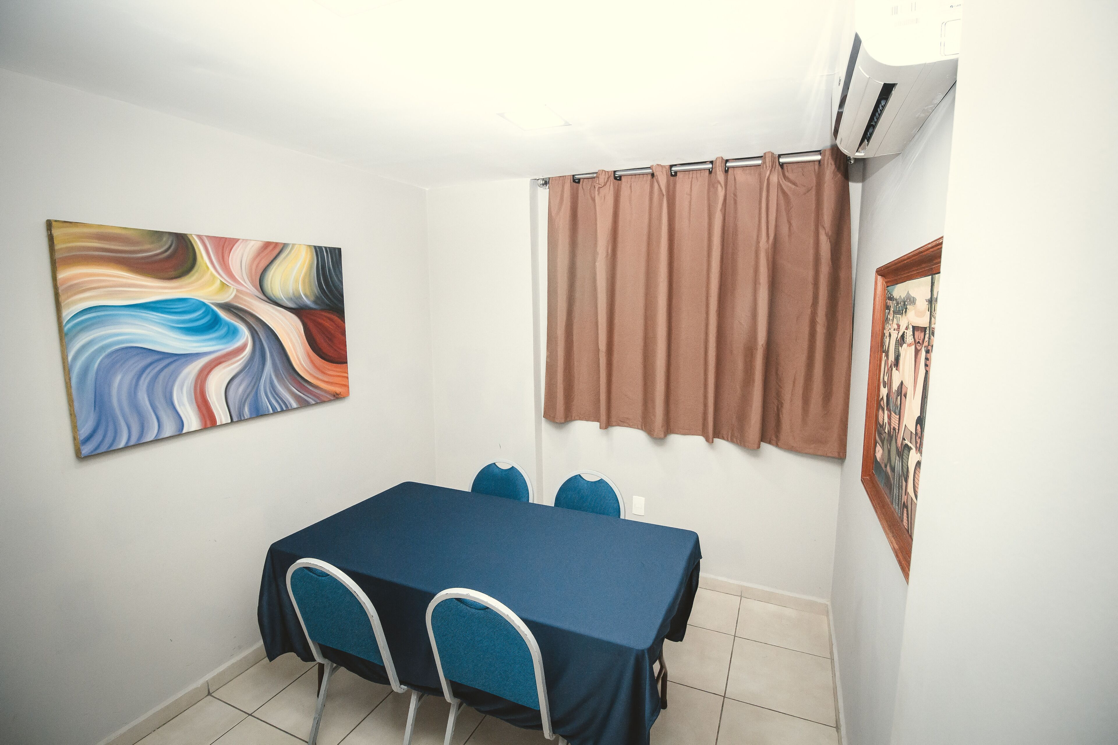 A dining area with a table, chairs, a painting, a curtain, and an air conditioning unit.