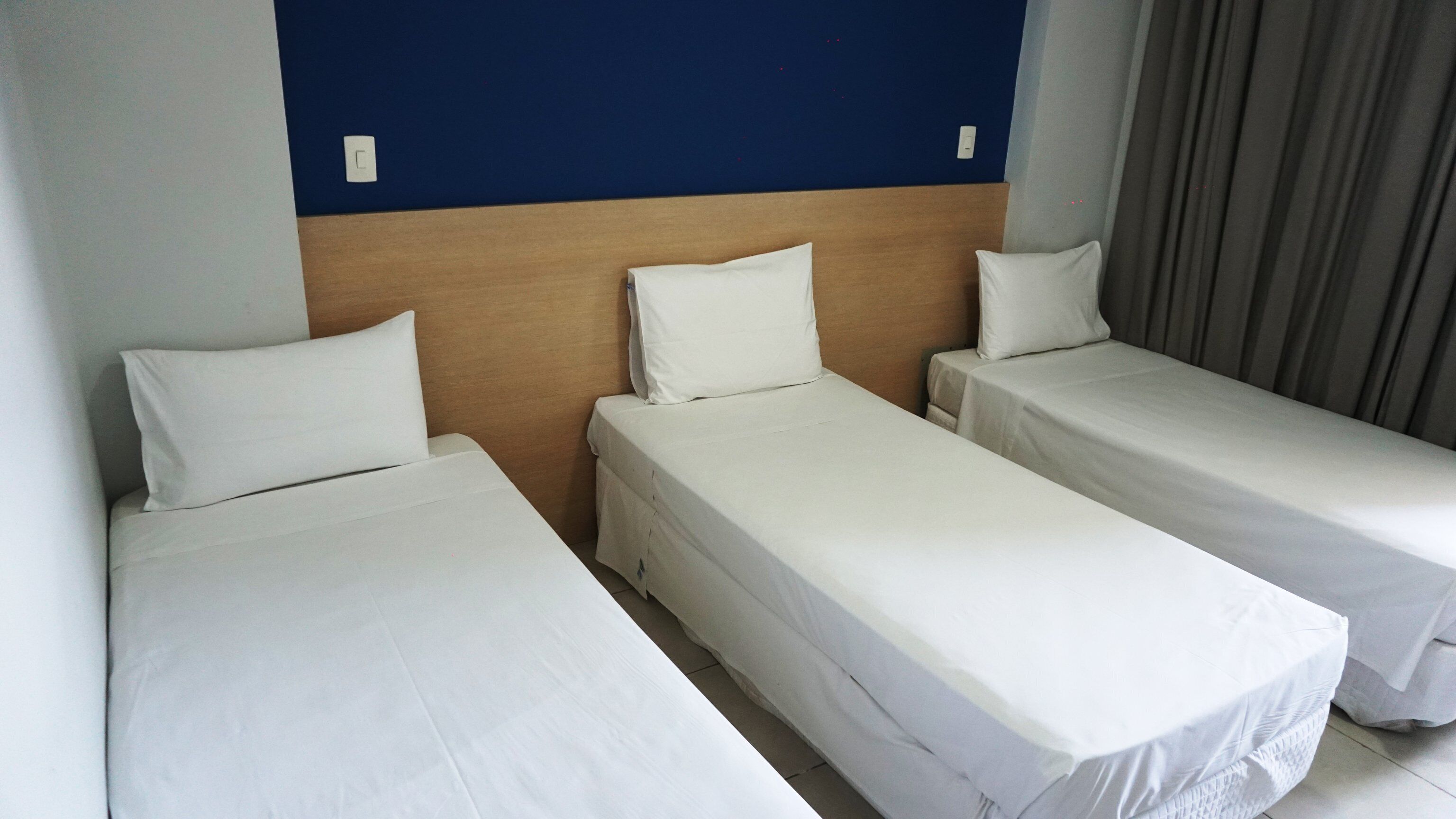 A hotel room with three single beds, a wooden headboard, and a blue accent wall.