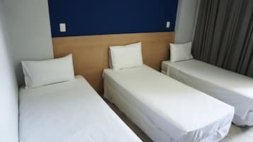 A hotel room with three single beds, a wooden headboard, and a blue accent wall.