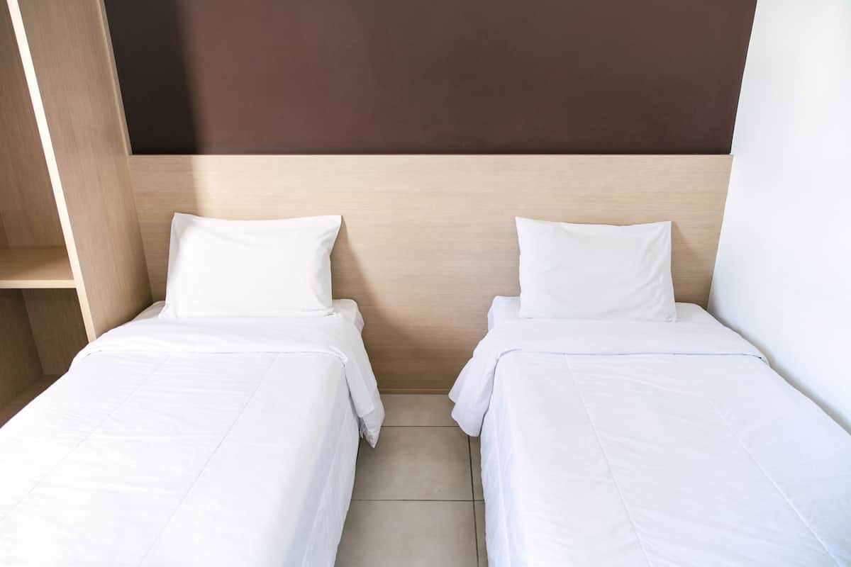 Two single beds with white linens in a room with wooden headboards and a brown accent wall.