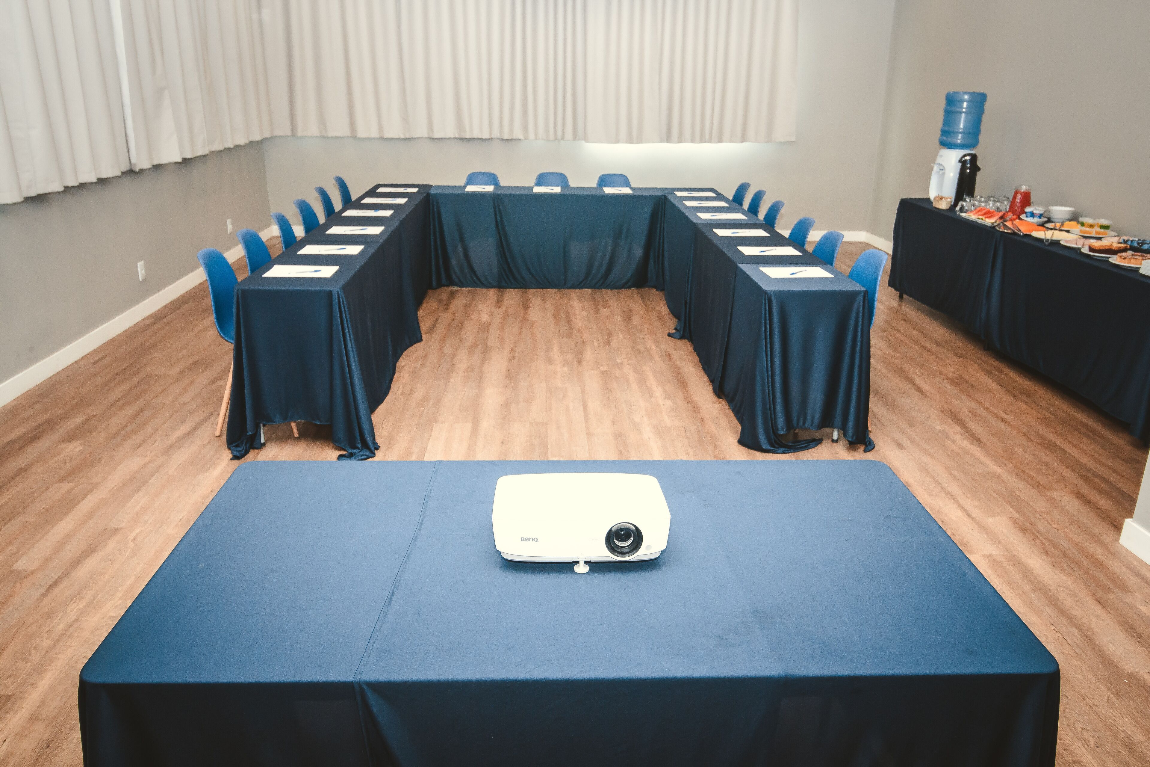 Un salón de conferencias con una larga mesa, sillas azules y un proyector sobre una mesa.