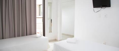 Habitación de hotel con dos camas, un televisor montado en la pared y un balcón accesible por una puerta corrediza.