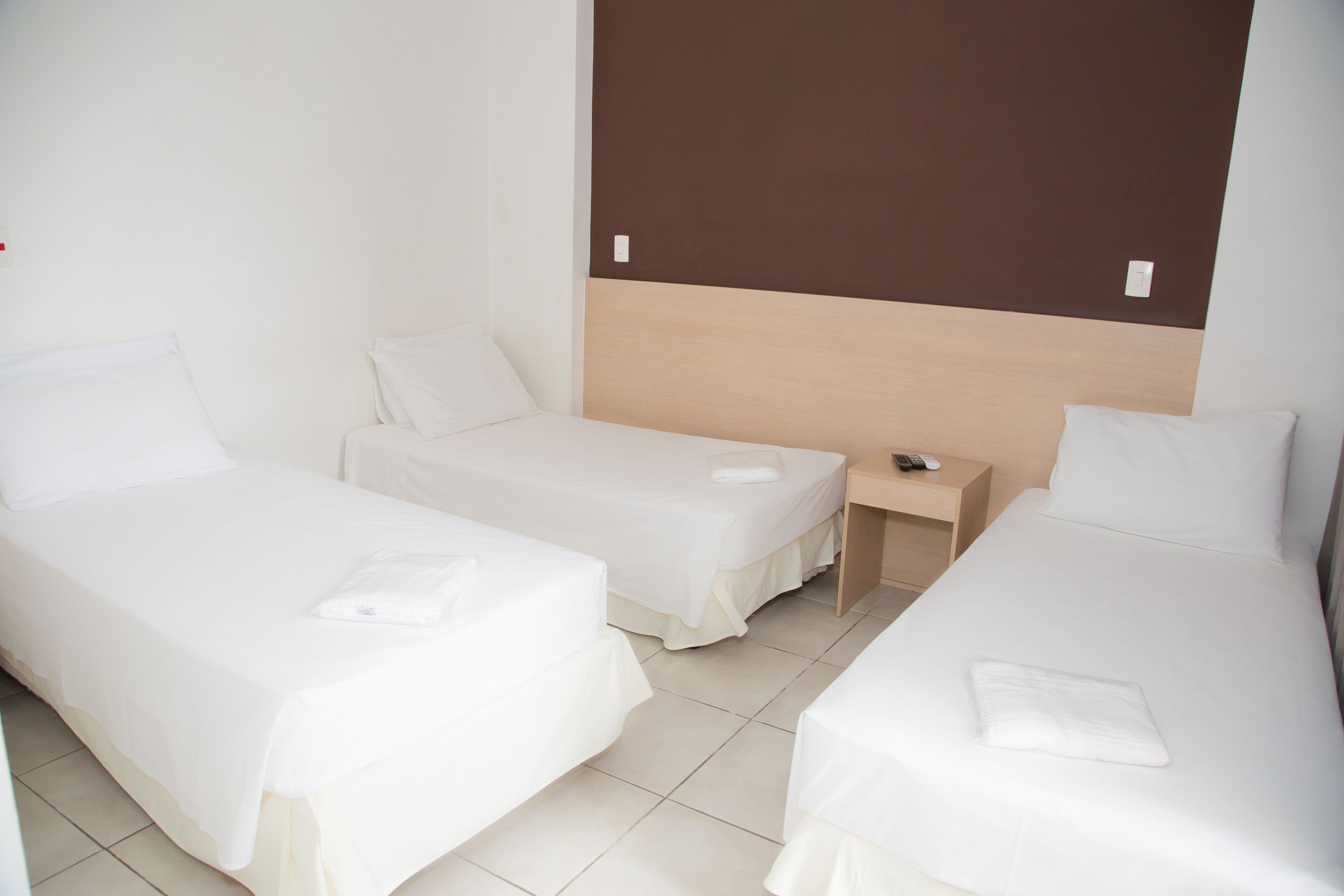 Una habitación de hotel con dos camas individuales, un cabecero de madera, una mesita de noche con un control remoto y una pared blanca.