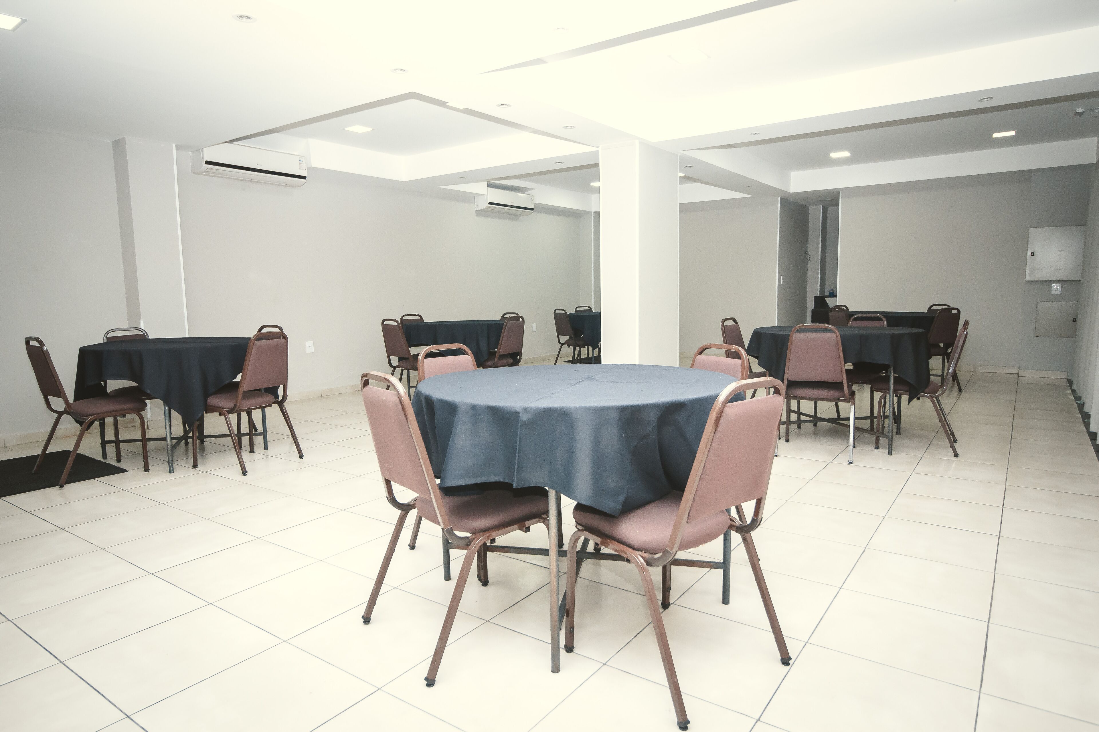 A conference room with round tables and chairs, white walls, and ceiling lights.