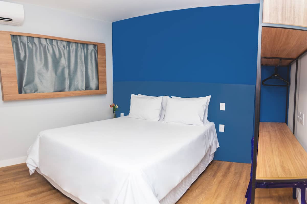 A neatly made bed with white linens in a room with blue walls and wooden flooring.