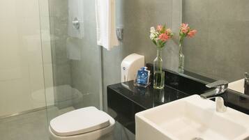 Un baño moderno con ducha de vidrio, inodoro blanco, lavabo negro y espejo.