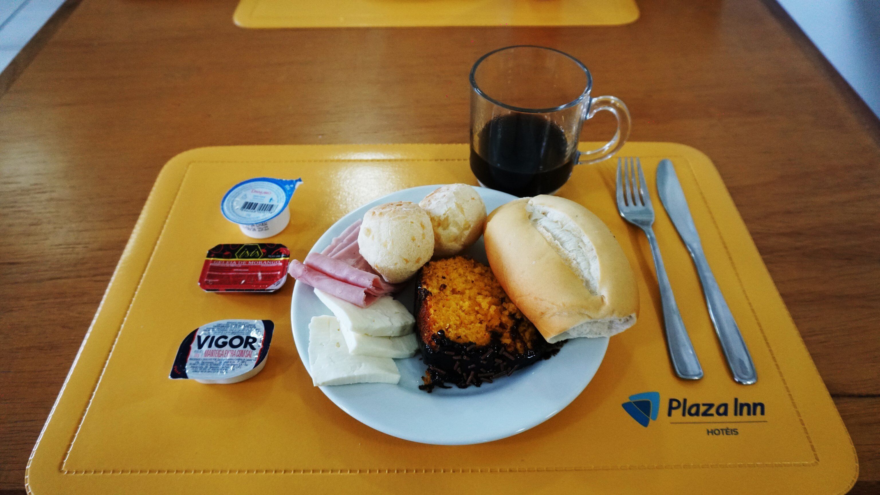 A meal tray with a plate of food, a glass of coffee, and condiments on a yellow placemat.