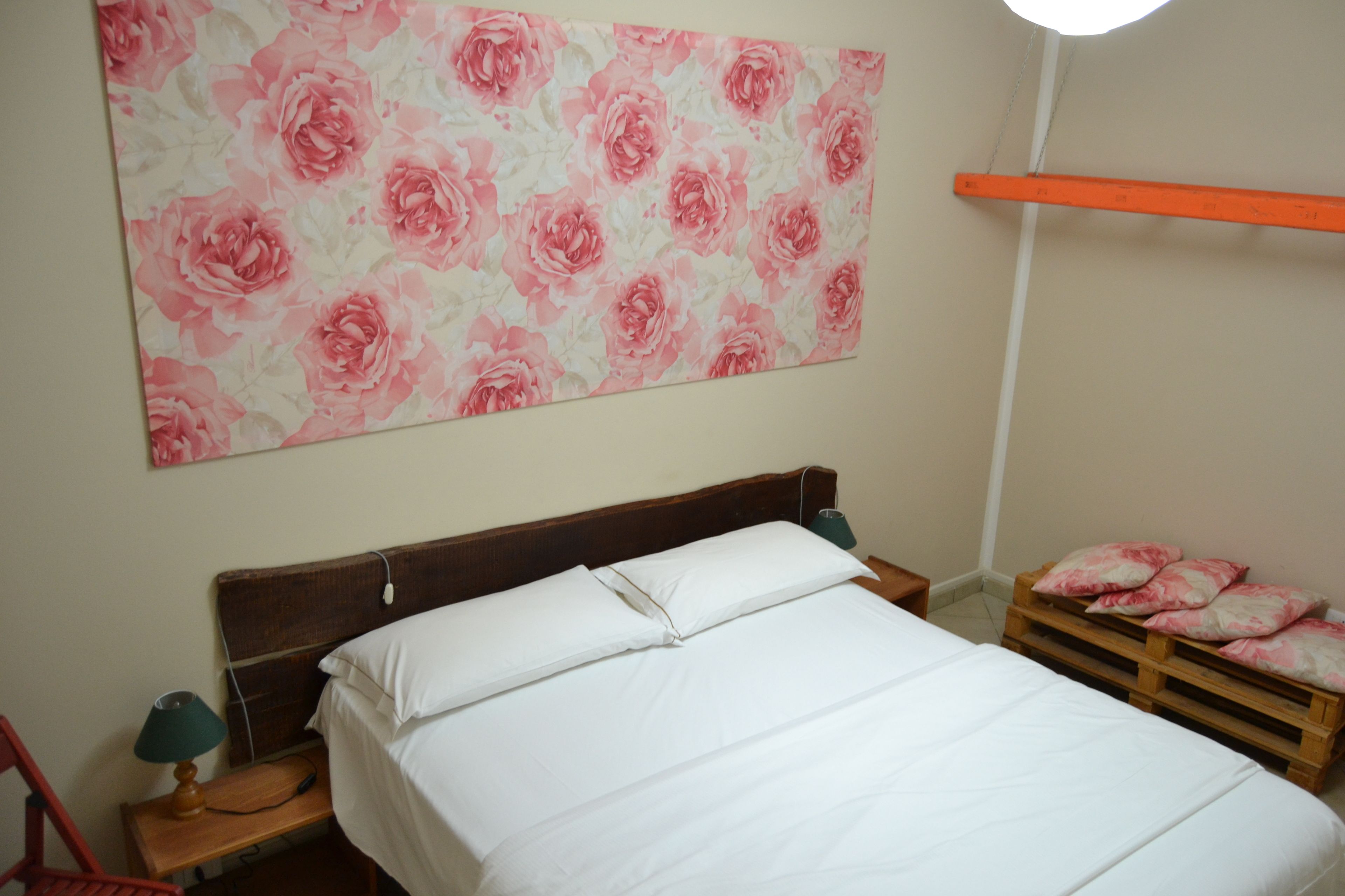 Un dormitorio con una cama de madera, ropa de cama blanca, un papel tapiz floral, una lámpara de noche y una mesita de noche de madera.
