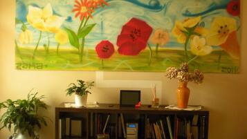A painting of flowers on a wall, a bookshelf with books and a small plant, and a vase with dried flowers on a table.