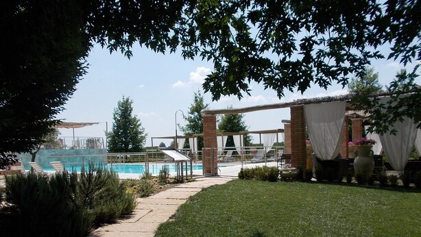 Un espace piscine doté d’un coin salon abrité, d’un mur en briques et d’une pelouse.