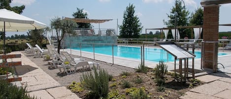 Zona de piscina con sillones de descanso, un espacio de estar cubierto y una vista despejada de la piscina.