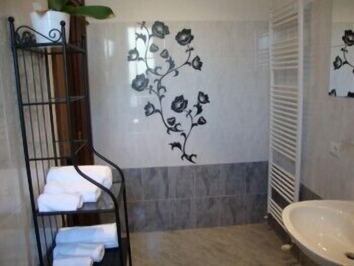 Een badkamer met een zwart metalen rek met handdoeken, een witte wastafel en een decoratieve wand met een bloemmotief.