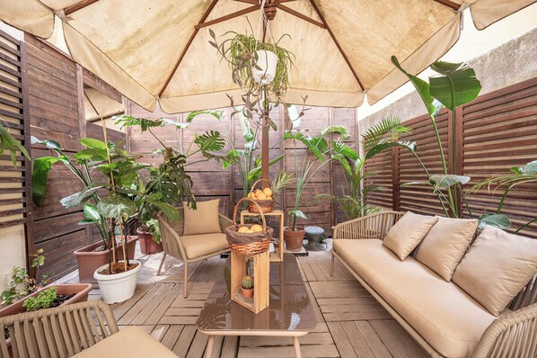 An outdoor patio with a wooden floor, wicker furniture, and various potted plants. - Corso Suite 107 Rooms Wellness & Spa (Rome)
