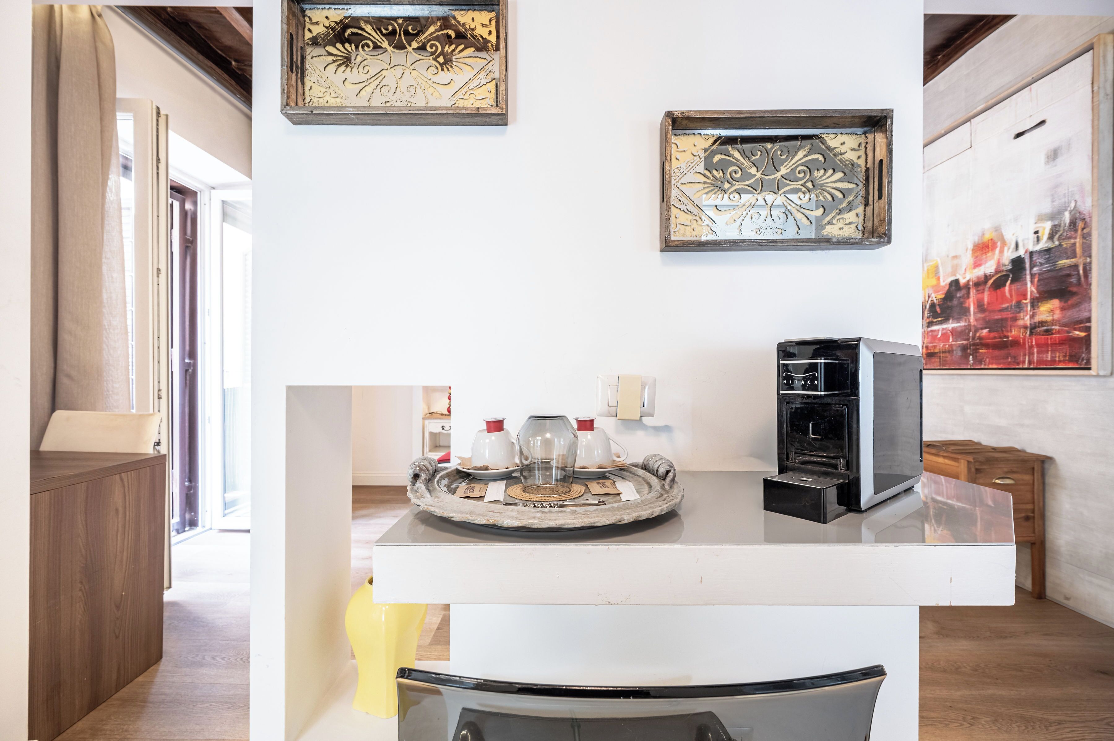 Une cuisine moderne équipée d’une machine à café, d’un plateau avec des tasses et une théière, ainsi que d’œuvres d’art décoratives murales.