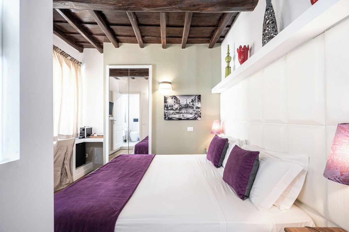 A bedroom with a bed, a desk, a chair, a window with curtains, a door, and a wall-mounted lamp.