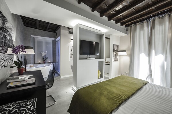 Habitació d'hotel moderna amb un llit, una taula de treball amb un ordinador, televisió i un bany amb banyera.