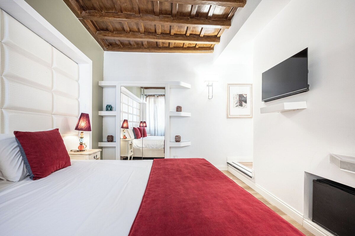 A modern bedroom with a large bed, a TV mounted on the wall, and a wooden ceiling.