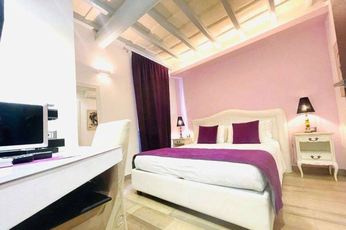 A bedroom with a bed, a desk, a TV, a lamp, and a nightstand.