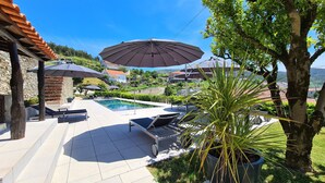 A pool area with lounge chairs and umbrellas, surrounded by greenery and a stone wall.