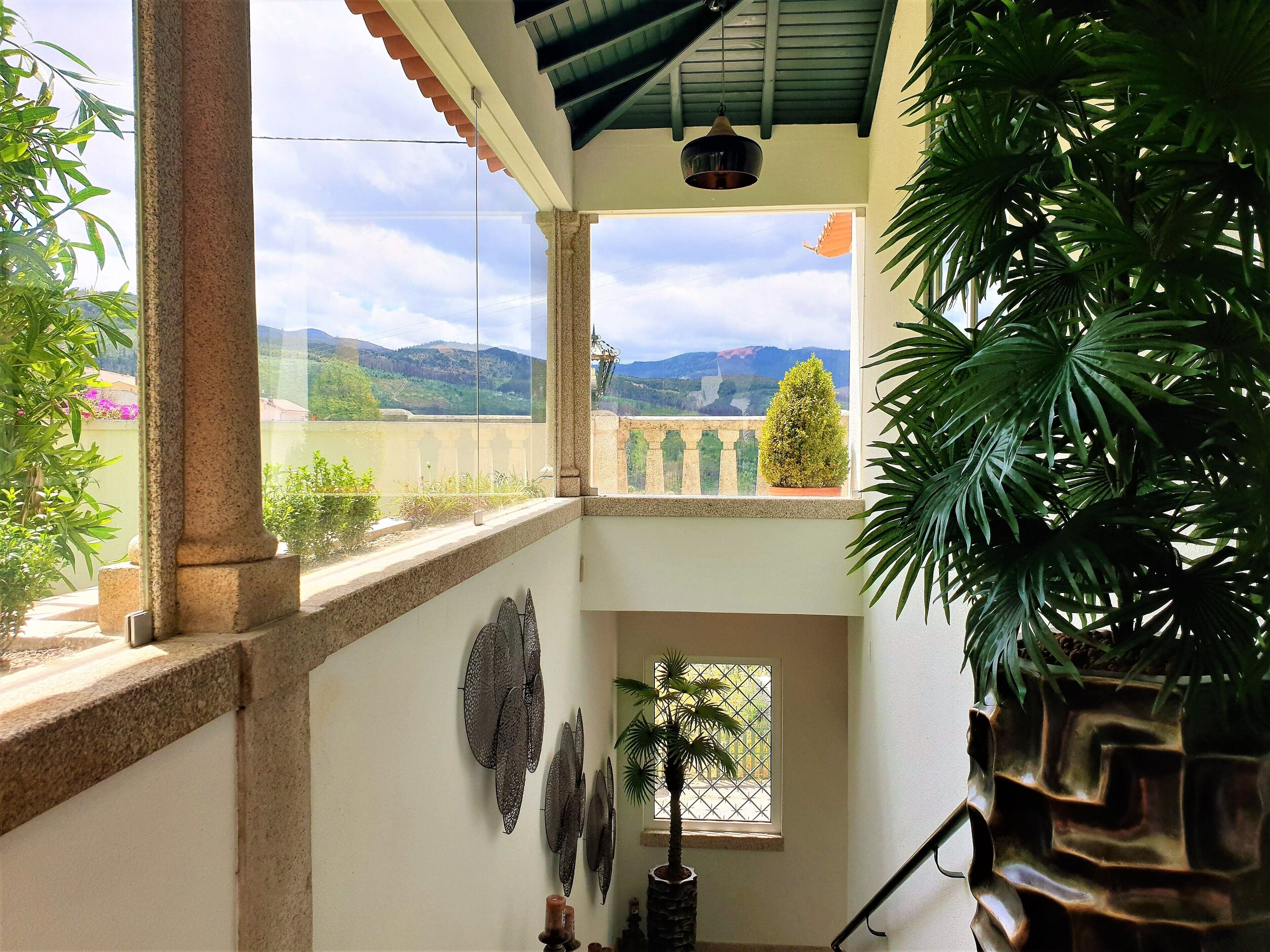 A balcony with a view of mountains, a potted plant, and decorative wall art.
