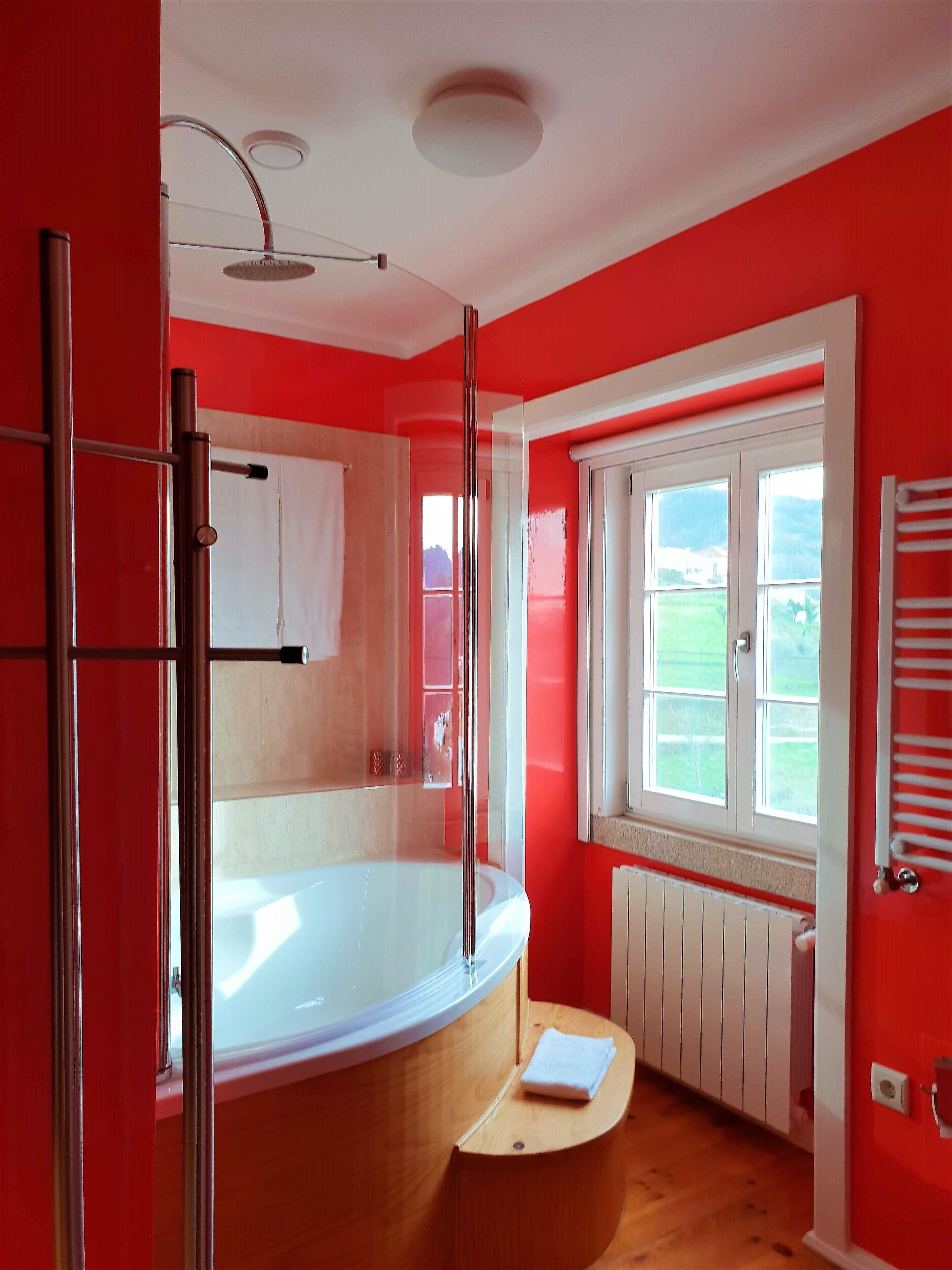 Ein modernes Badezimmer mit einer Duschkabine, einer Badewanne und einem Fenster mit Blick auf Grünflächen.