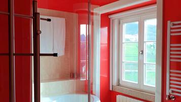 Ein modernes Badezimmer mit einer Duschkabine, einer Badewanne und einem Fenster mit Blick auf Grünflächen.