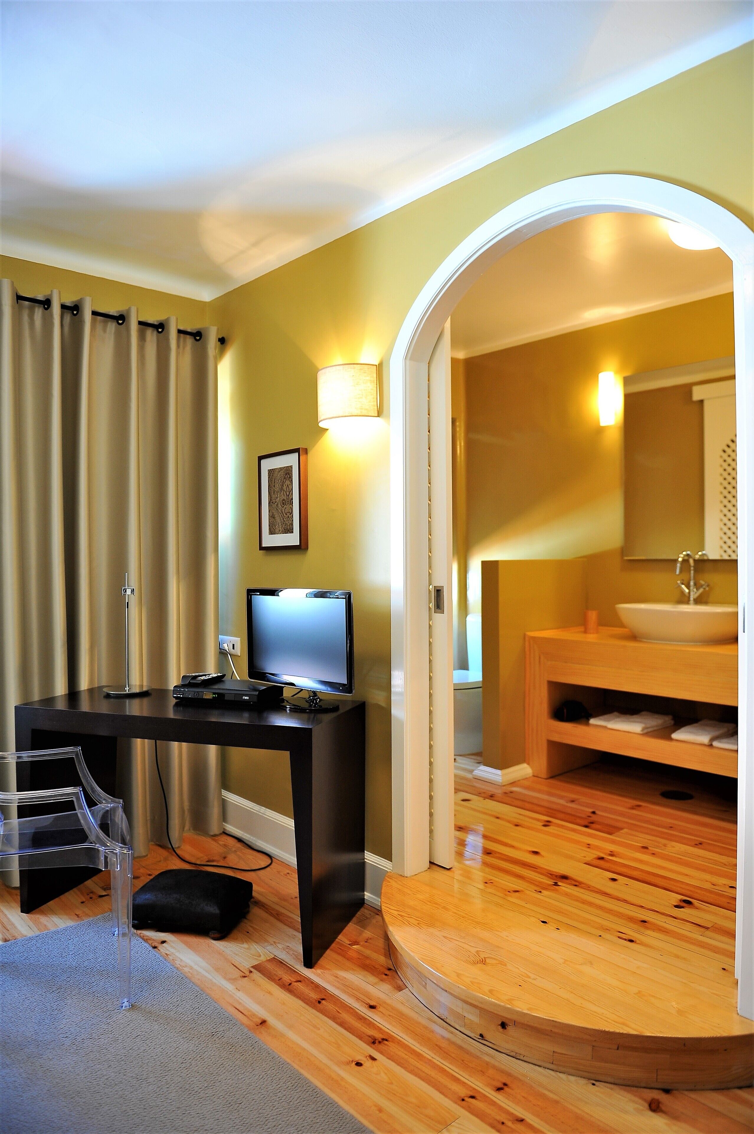 A hotel room with a desk, computer, and a bathroom with a sink and mirror.
