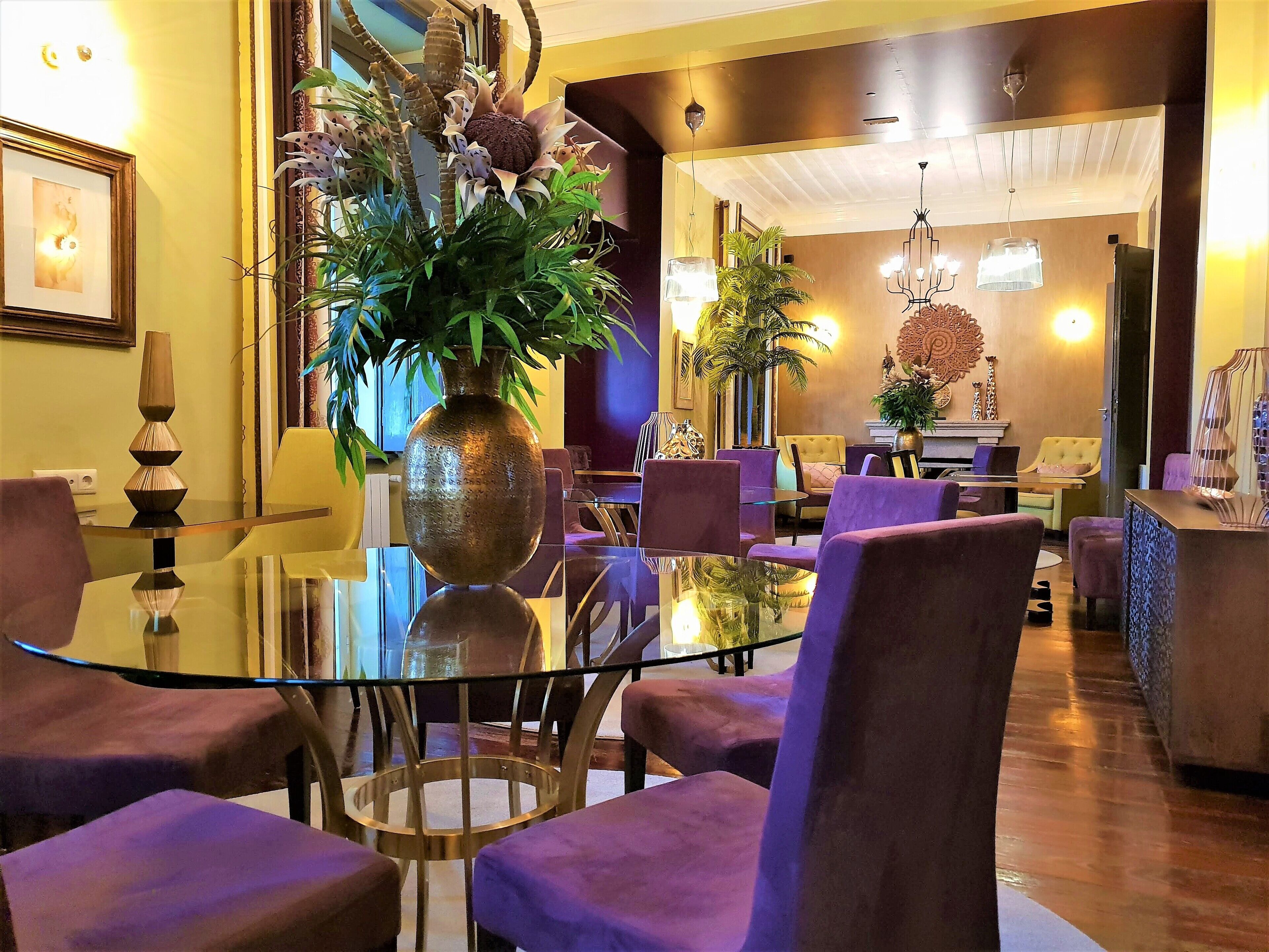 Un hall d’hôtel moderne avec une table en verre, des fauteuils recouverts d’un tissu violet et une grande plante décorative.
