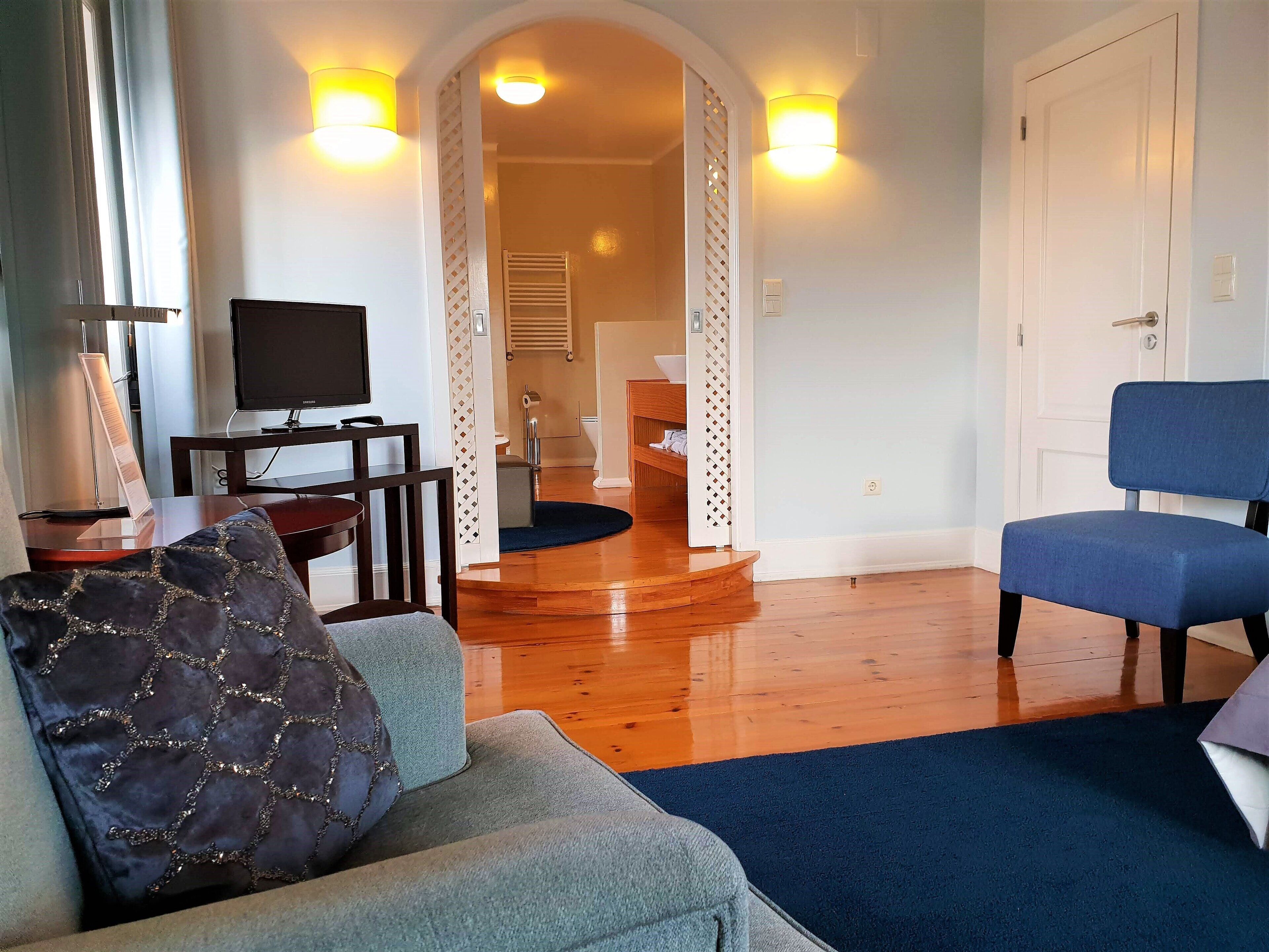 A living room with a sofa, a blue chair, a television, and a small table with a lamp.