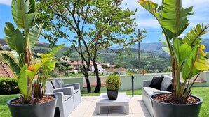 A patio with outdoor furniture and large potted plants, overlooking a scenic landscape.