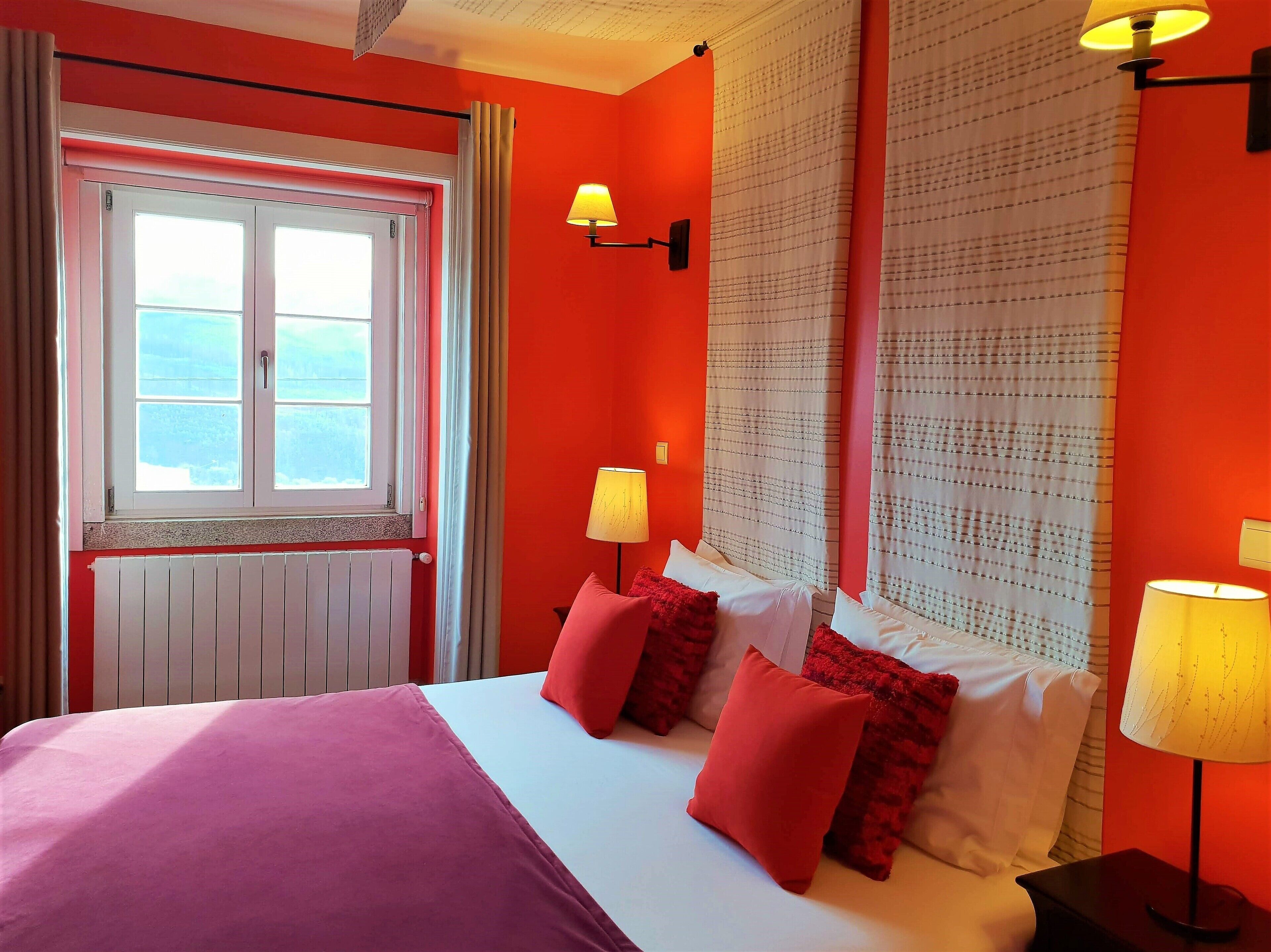A room with a bed, two bedside lamps, a window, and curtains.