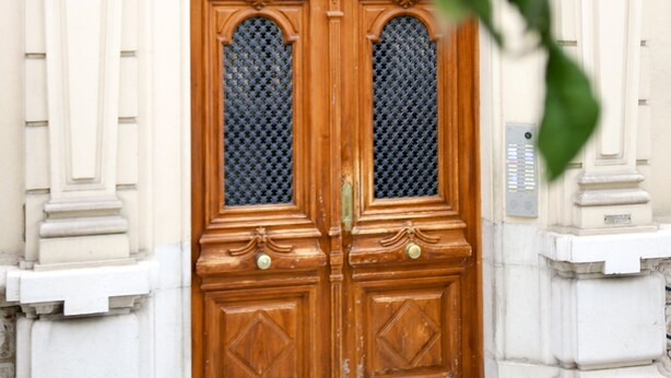 Una puerta doble de madera con paneles de vidrio, ubicada en un estilo arquitectónico clásico con detalles ornamentales y un letrero arriba que dice "Palais Yolande".